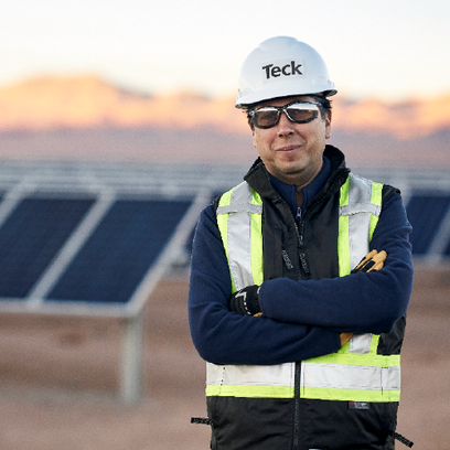 Man in safety gear stands confidently in front of a solar panel field at sunset.